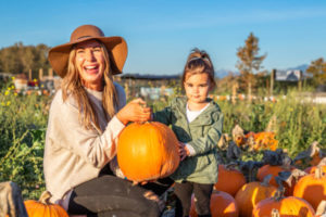 Woman wearing hat and weilding pumpkin, small girl standing next to her in pumpkin patch at Stocker Farms