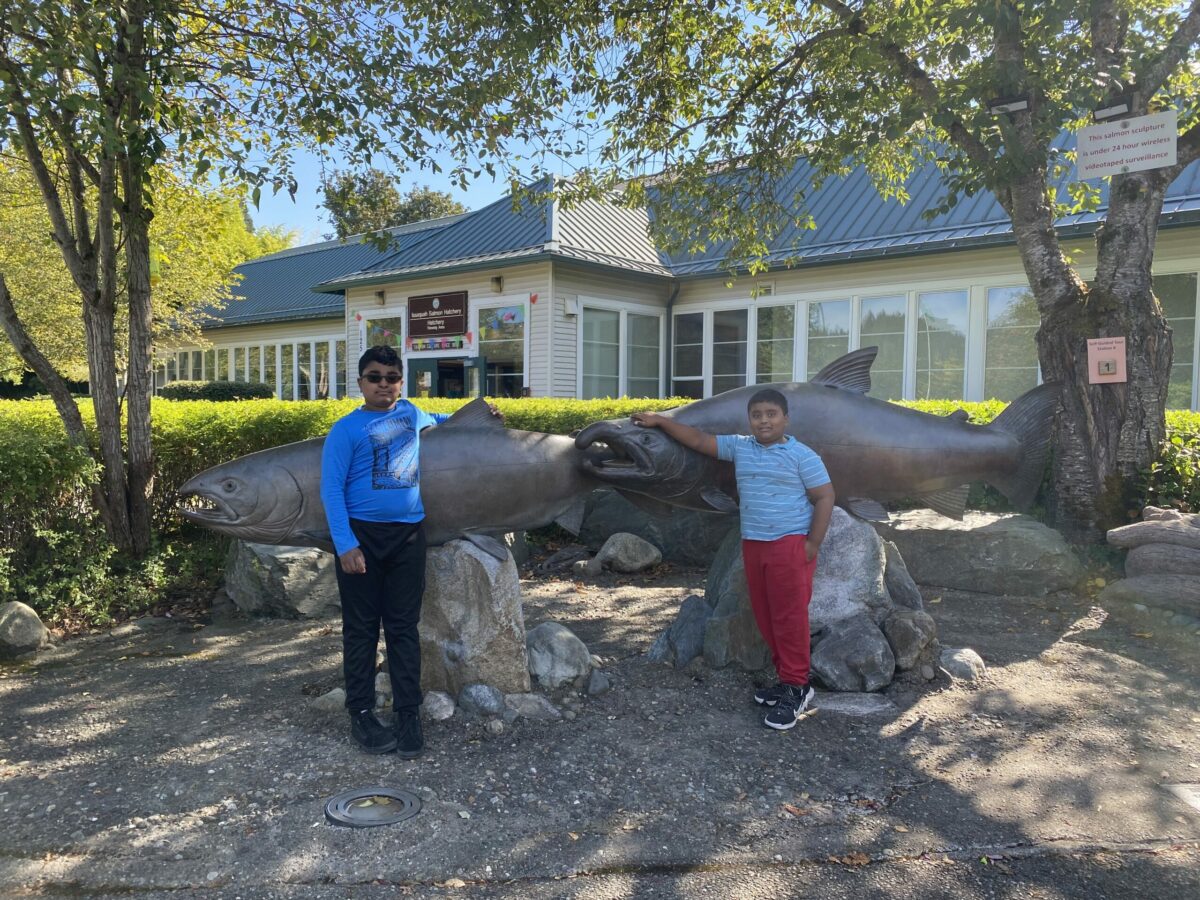 Two children stand in front of tall salmon statues at the Issaquah Salmon Hatchery.