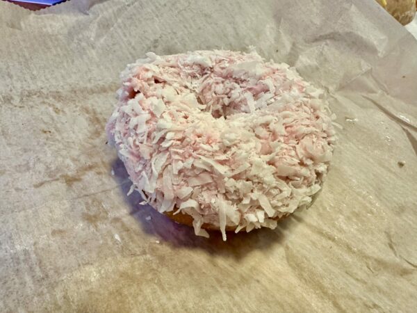 Doughnut covered in pink frosting and white coconut flakes. 