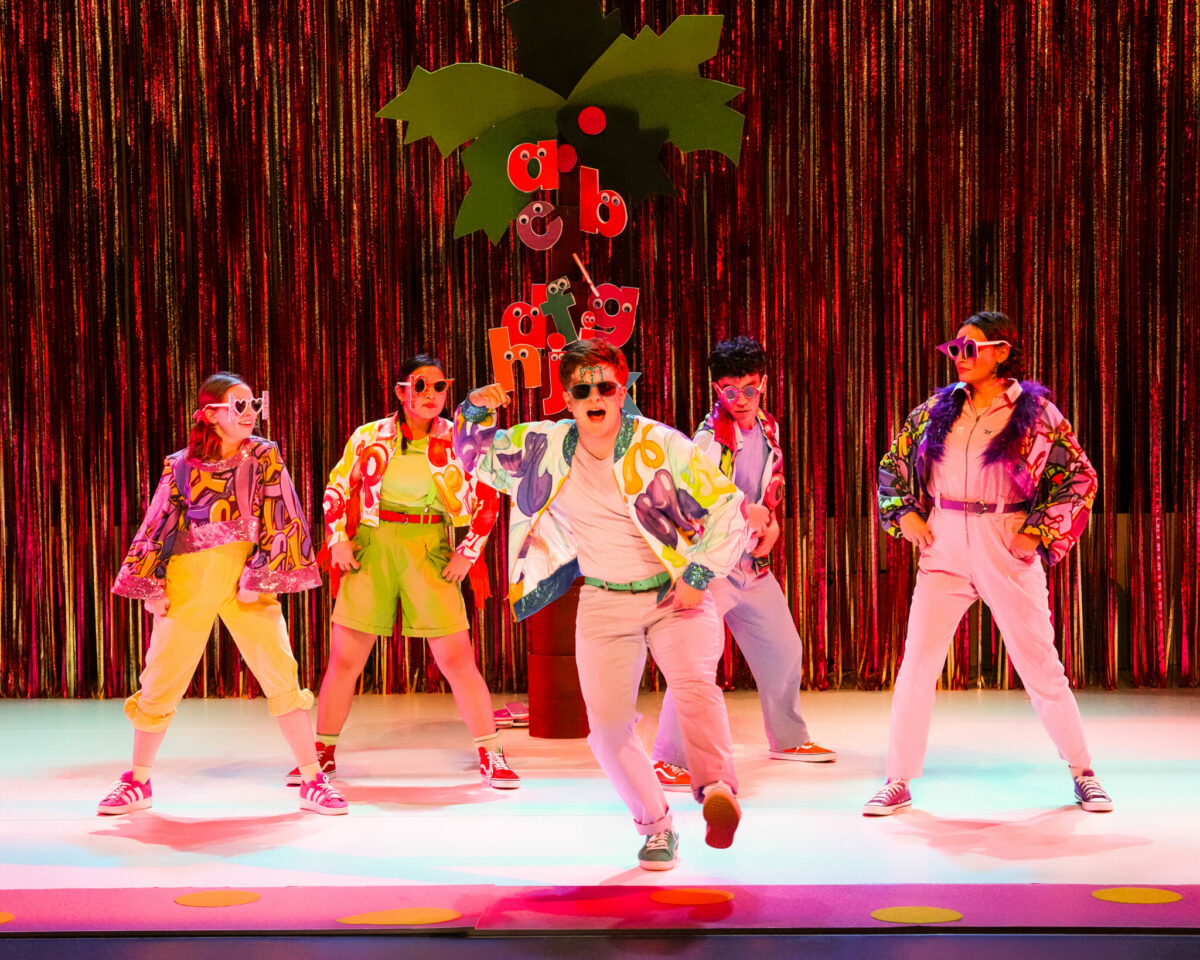 Cast members in colorful jackets and sunglasses dance in front of a glitter curtain in Chicka Chicka Boom Boom: The Musical at Seattle Children’s Theatre.