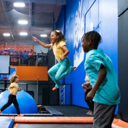Kids jumping on trampolines at an indoor Sky Zone park with padded walls and bright play features.