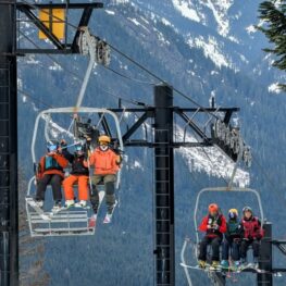 Families riding a chairlift at the Summit at Snoqualmie on a winter day, with skiers and snowboarders bundled in colorful gear and the snow-covered Cascade Mountains rising behind them.